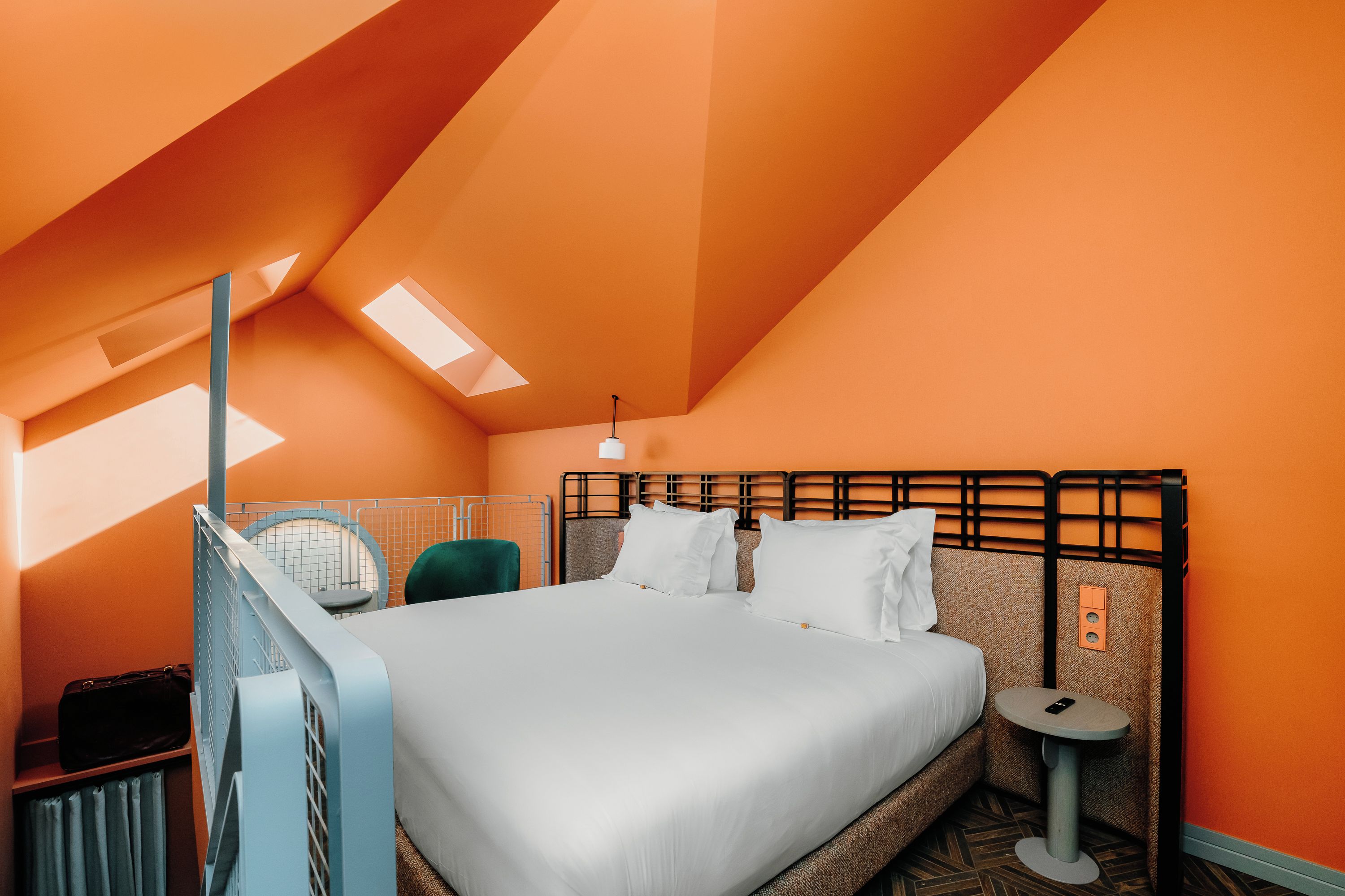 A hotel room with a bed, a bedside table, a chair, and a small table with a phone.