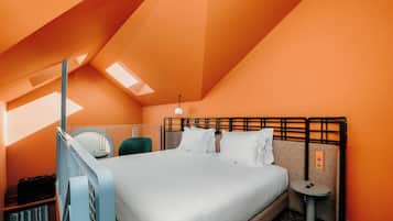 A hotel room with a bed, a bedside table, a chair, and a small table with a phone.