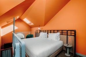 Una habitación de hotel con cama, mesita de noche, una silla y una pequeña mesa con un teléfono.