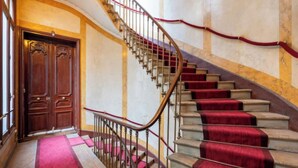 Un grand escalier recouvert d’une moquette rouge, avec une porte en bois au bas.