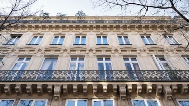 Un immeuble à plusieurs étages de style architectural classique, doté d’un balcon orné de balustrades décoratives.