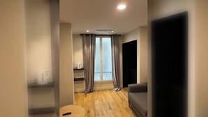Un salon moderne avec un plancher en bois, un canapé gris, une table basse et une grande fenêtre avec des rideaux.