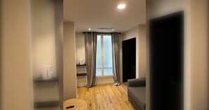 Ein modernes Wohnzimmer mit Holzboden, einem grauen Sofa, einem Couchtisch und einem großen Fenster mit Vorhängen.