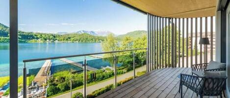 A balcony with a view of a lake and mountains, a chair, and a lamp.