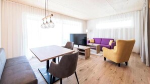 Un salon moderne avec un plancher en bois, une table à manger, un canapé, un téléviseur et une lampe.
