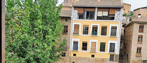 A multi-story building with a yellow facade, a stone base, and a small courtyard with a pond.