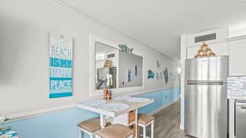 A kitchen with a stainless steel refrigerator, a white table with two chairs, and a wall with a beach-themed sign.