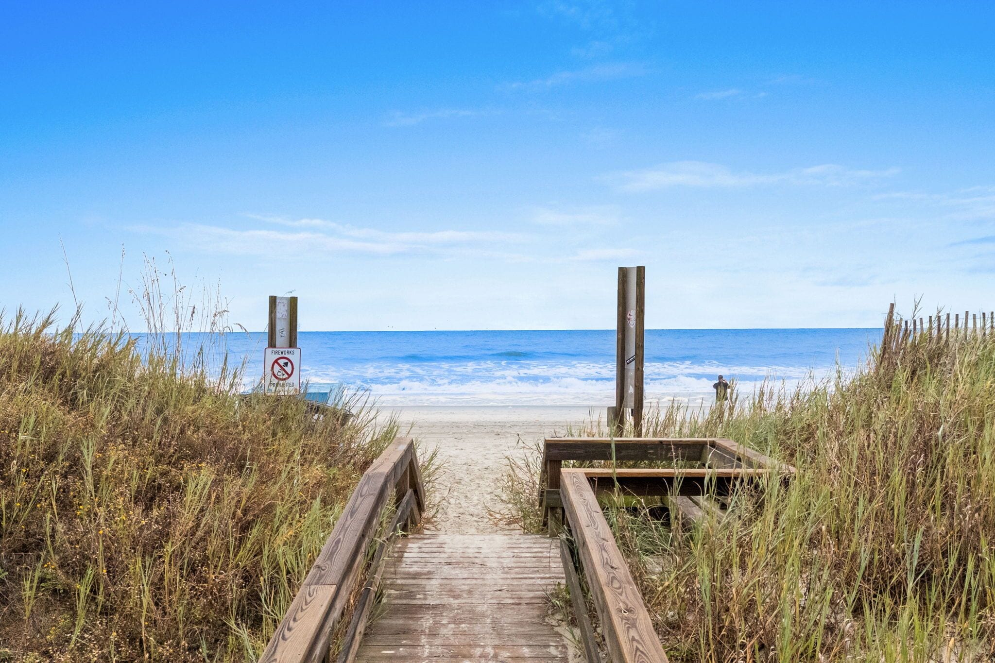 A wooden pathway leading to a beach with a no swimming sign.