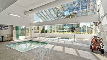 An indoor swimming pool with clear glass walls, a lifeguard sign, and a hose reel on the right.