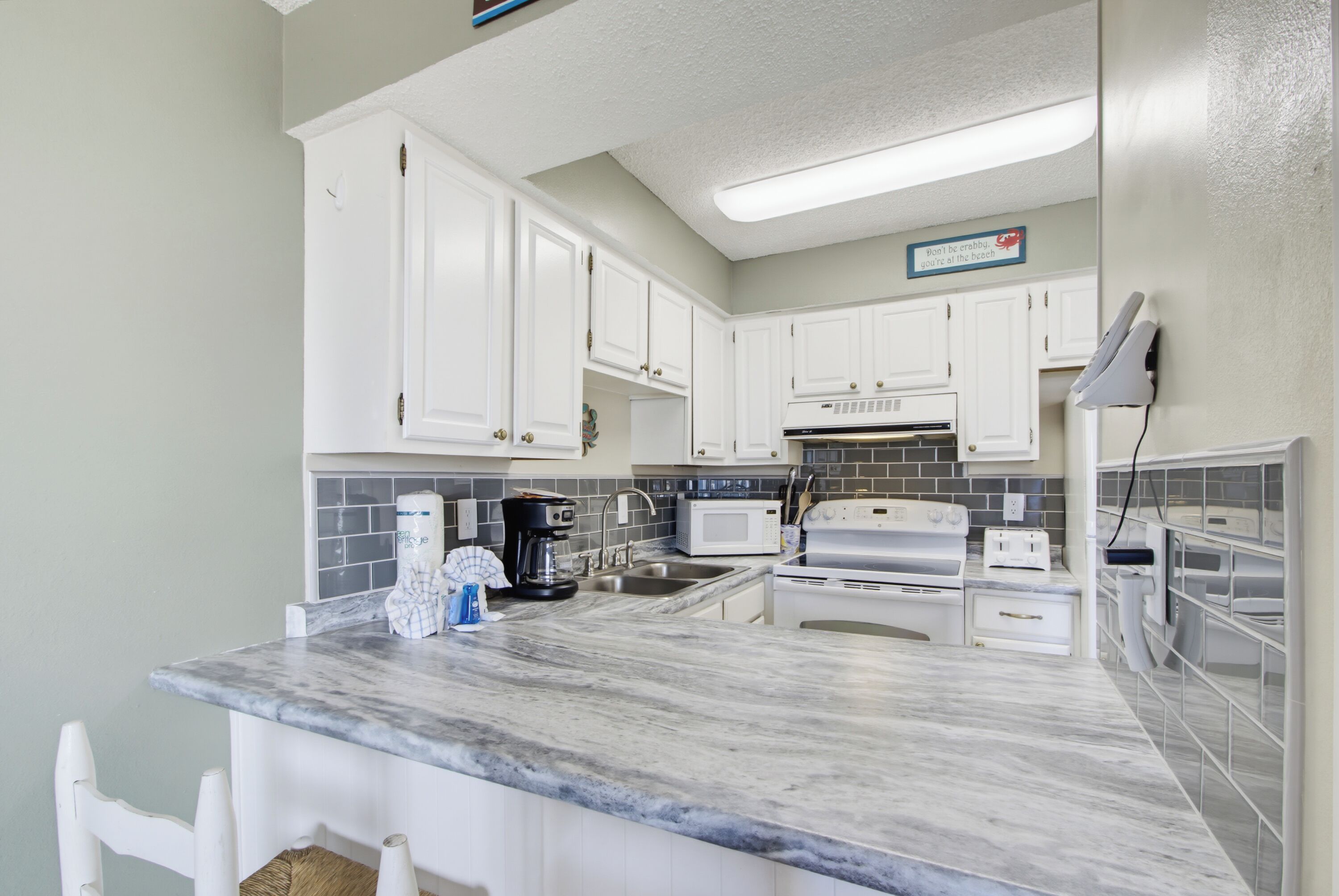 A kitchen with white cabinets, a marble countertop, a coffee maker, a microwave, and a stove.