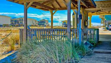 A beachside wooden structure with a deck, surrounded by tall grasses and a clear sky.
