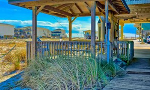 Eine Holzkonstruktion am Strand mit einer Terrasse, umgeben von hohen Gräsern und blauem Himmel.