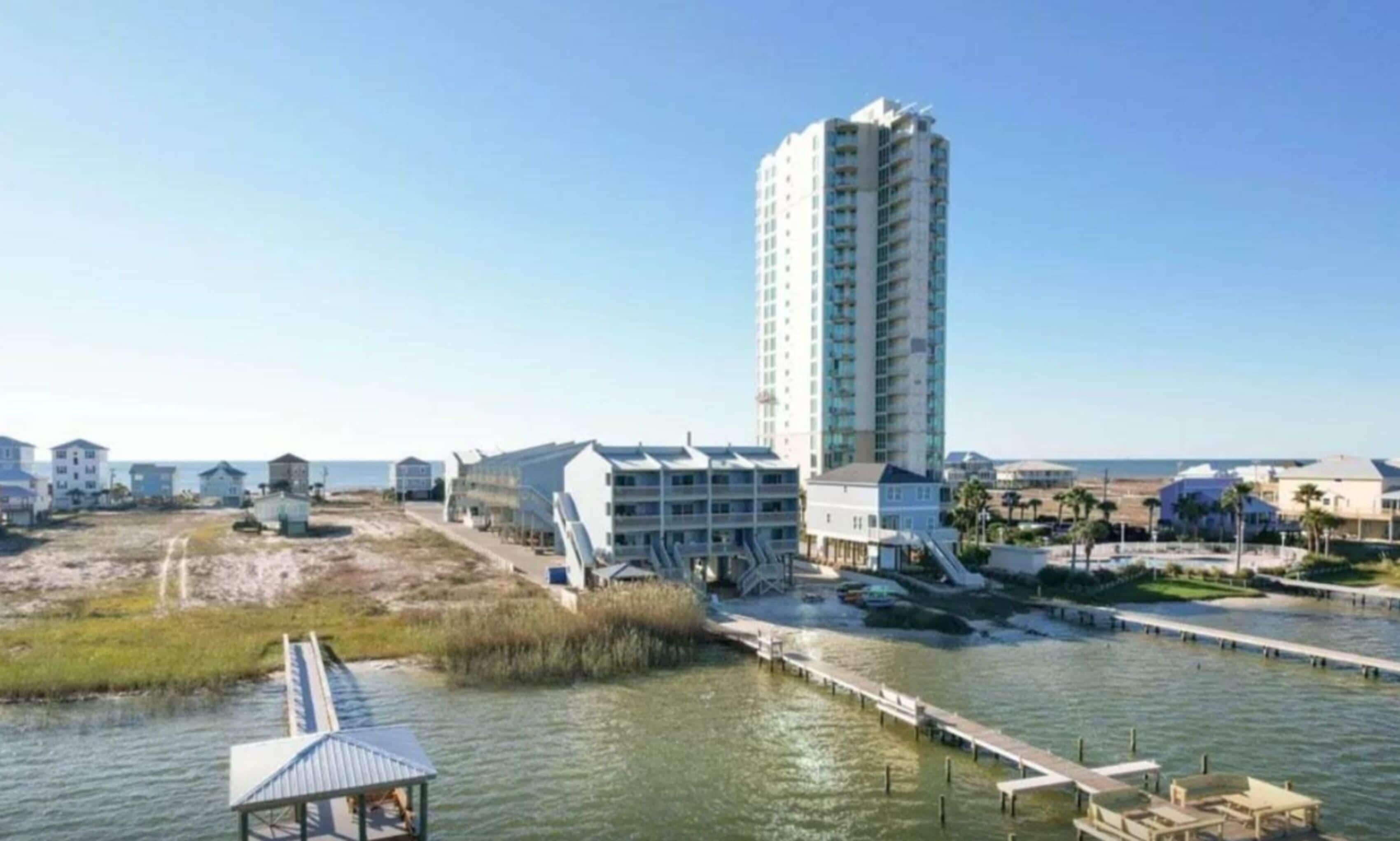 A coastal hotel with a tall building, a pier, and a beach area.
