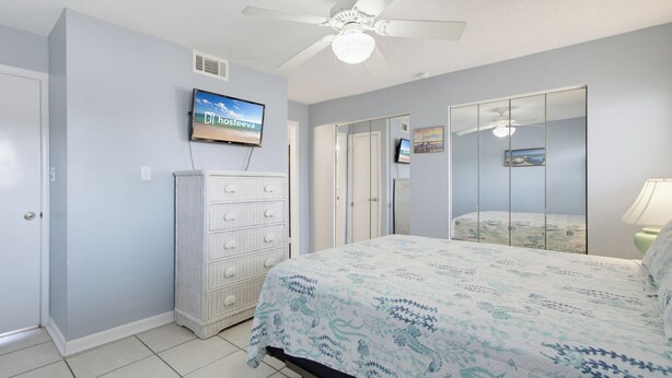A bedroom with a bed, a dresser, a television, and a ceiling fan.
