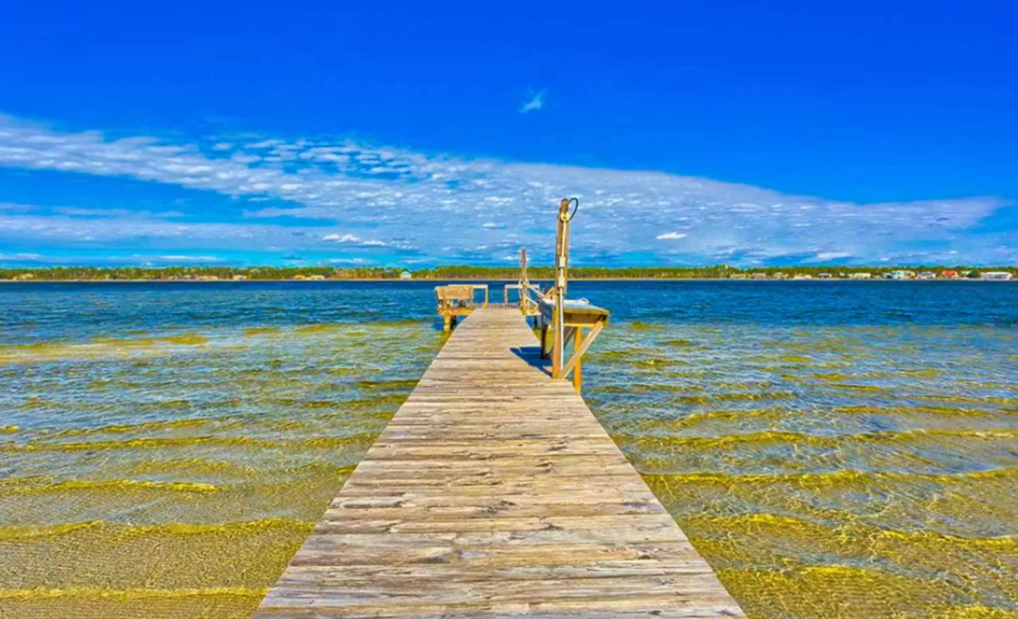 Un muelle de madera que se extiende sobre un mar azul y transparente, con una costa distante.