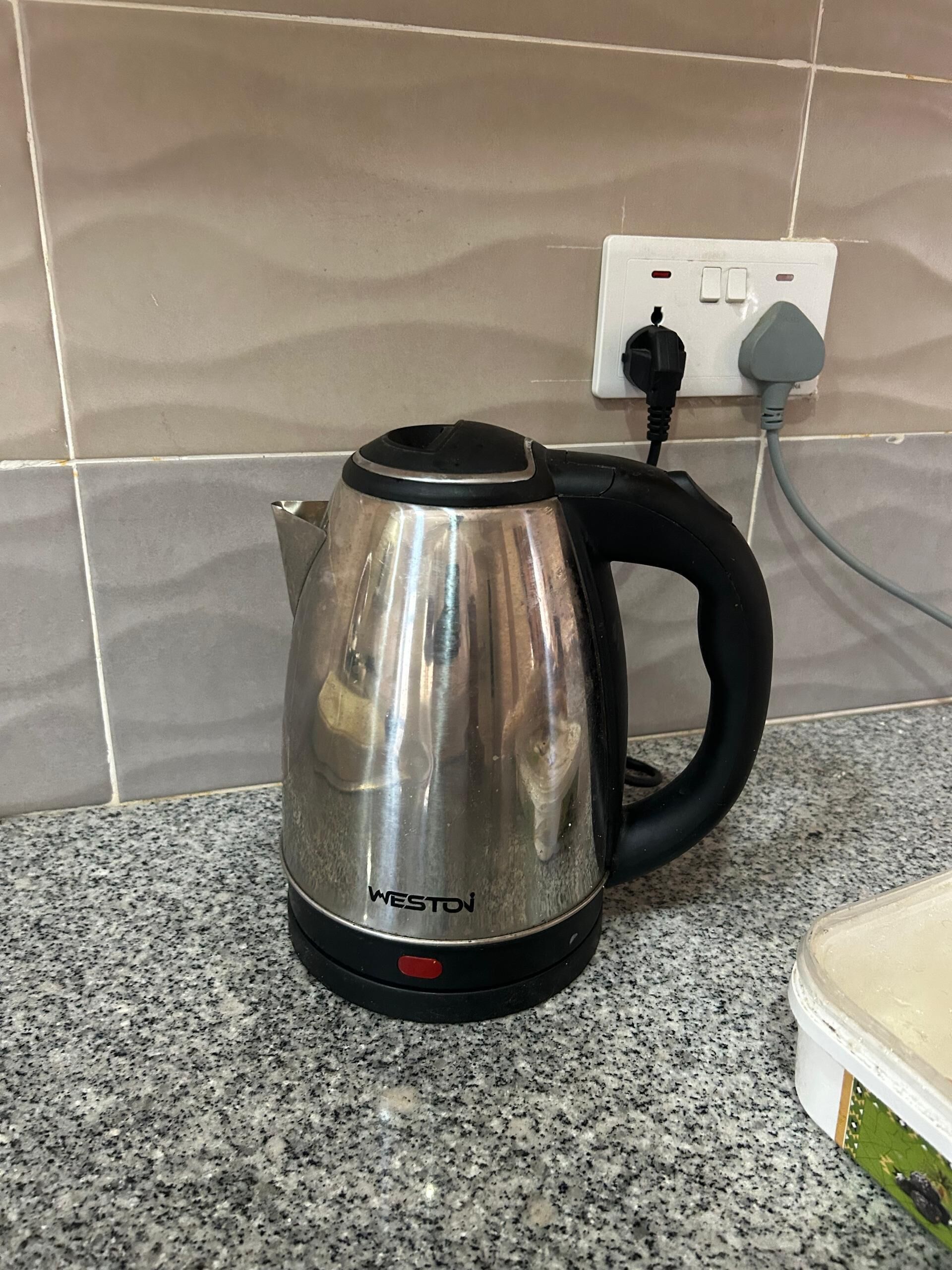 Una tetera de acero inoxidable con un asa negro y el nombre de marca 'WESTOJ' sobre una encimera de granito.