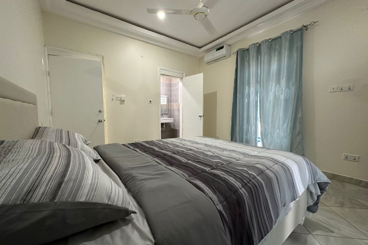 A bedroom with a bed, a ceiling fan, a window with curtains, and a door.