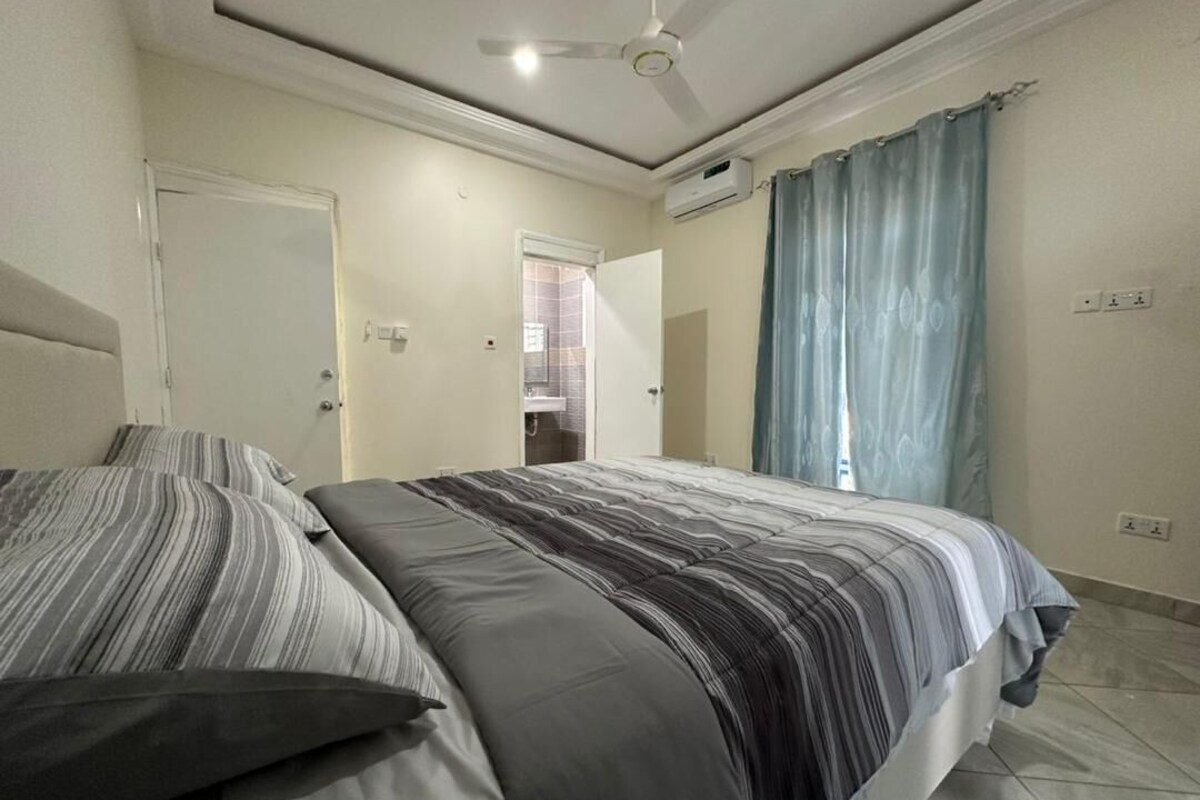 A bedroom with a bed, a ceiling fan, an air conditioning unit, and a bathroom door.