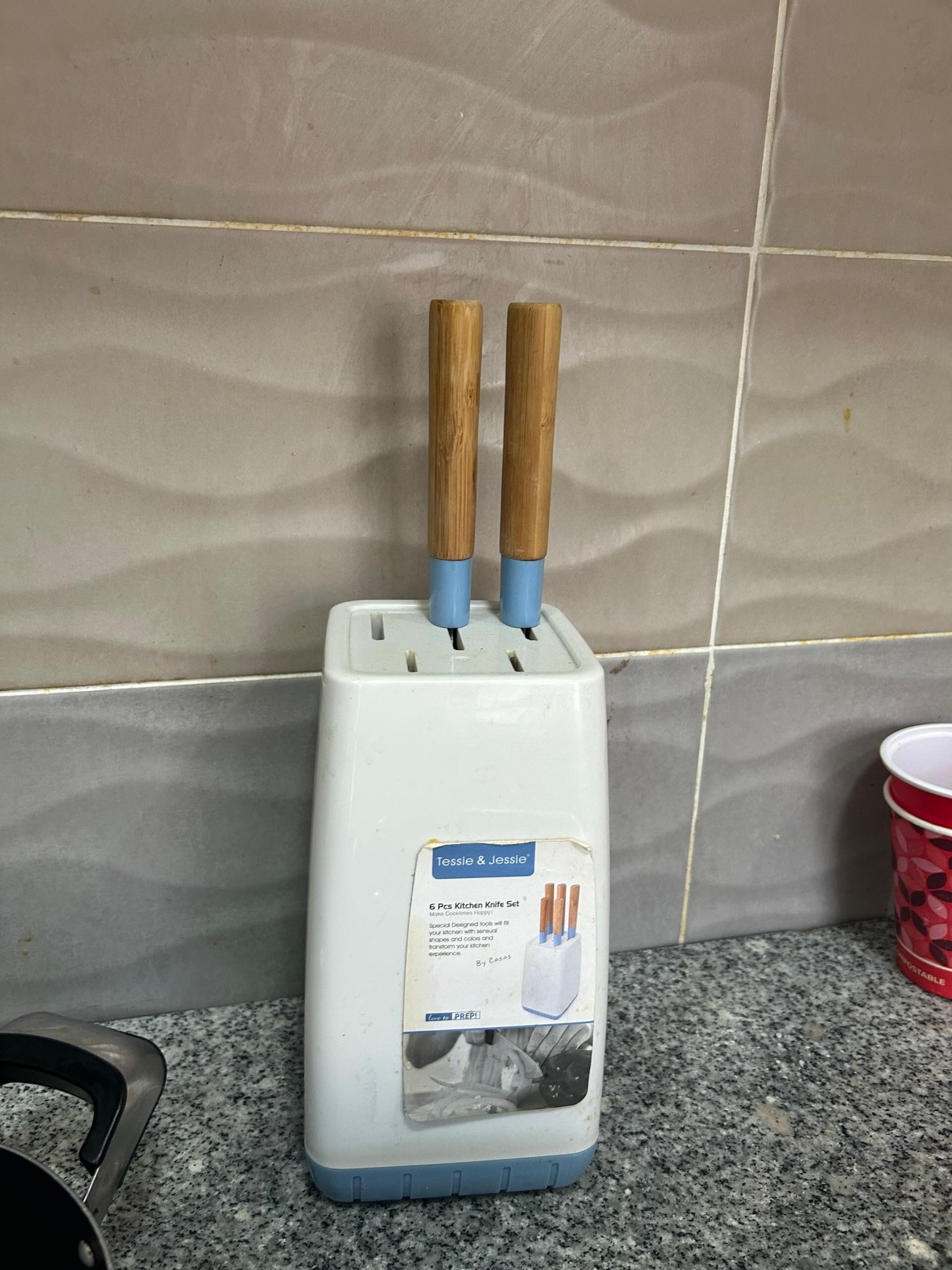 Een keukenapparaat met houten handgrepen, een label dat aangeeft dat het een messen set is, en een rode beker op het aanrecht.