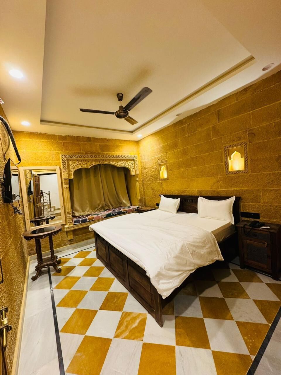 A hotel room with a large bed, a ceiling fan, a checkered floor, and a brick wall.