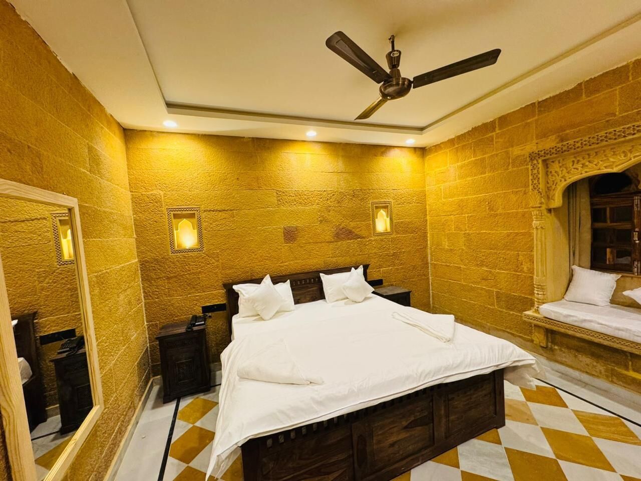 Quarto de hotel com uma cama grande, um ventilador de teto e piso quadriculado.