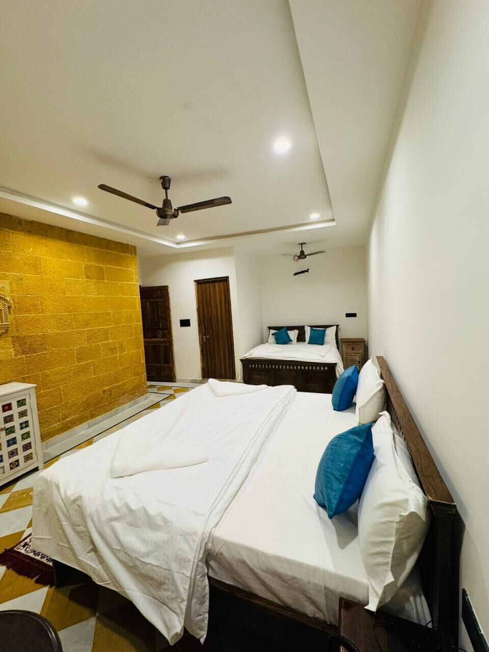 A hotel room with a bed, a ceiling fan, a wooden wall, and a door.
