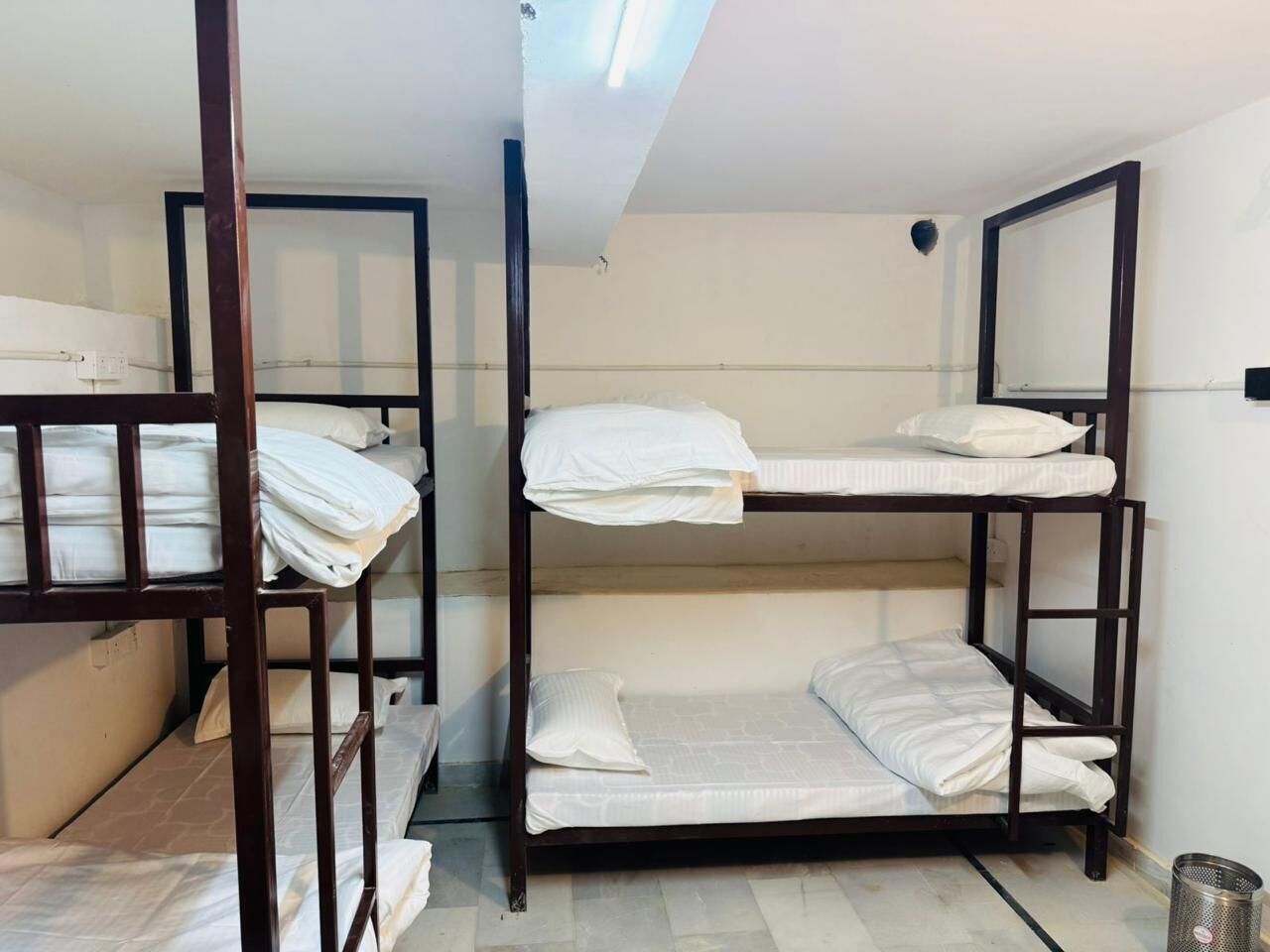 A room with bunk beds, a metal trash can, and a ceiling light fixture.