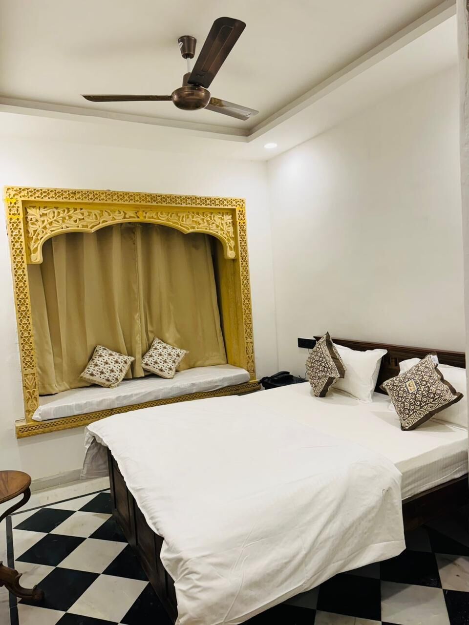 A hotel room with a bed, a ceiling fan, a decorative headboard, and a checkered floor.