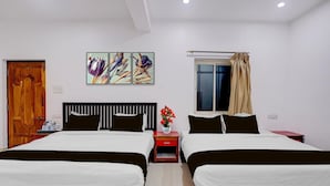 A hotel room with two beds, a wooden door, a window with curtains, and a wall-mounted artwork. - Deluxe Room Ravai (Calangute)