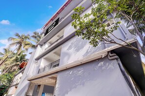 Ein Hotel mit Balkon, einem Hinweisschild, das es als Hotel kennzeichnet, und einem Baum im Vordergrund.