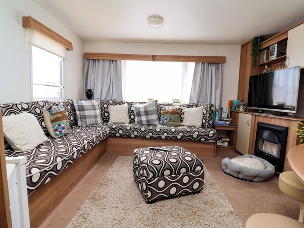 A modern living room with a sectional sofa, ottoman, and a flat-screen TV. - Pathway to the sea (Prestatyn)