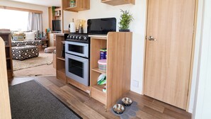 A compact kitchen with a stove, oven, and wooden shelving.