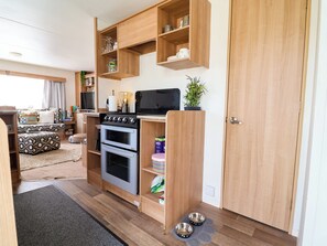 A compact kitchen with a stove, oven, and wooden shelving.