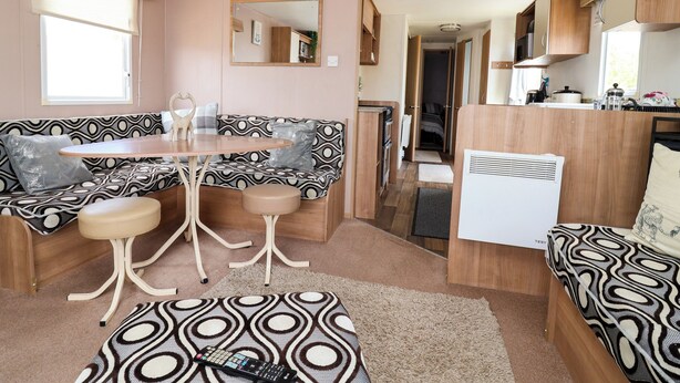 En kompakt autocamper-indretning med et tekøkken, et spiseområde med bord og stole, samt en opholdsstue med en sofa med mønster.