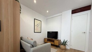 A modern living room with a grey sofa, a TV on a wooden stand, and a white door. - Apartment Quart Mid-stay (Valencia)