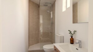 A modern bathroom with a glass-enclosed shower, a white toilet, and a sink with a mirror above. - Apartment Quart Mid-stay (Valencia)