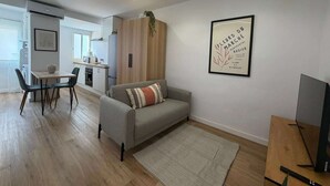 A modern living room with a grey sofa, a dining area with a table and chairs, a kitchen in the background, and a framed artwork on the wall. - Apartment Quart Mid-stay (Valencia)