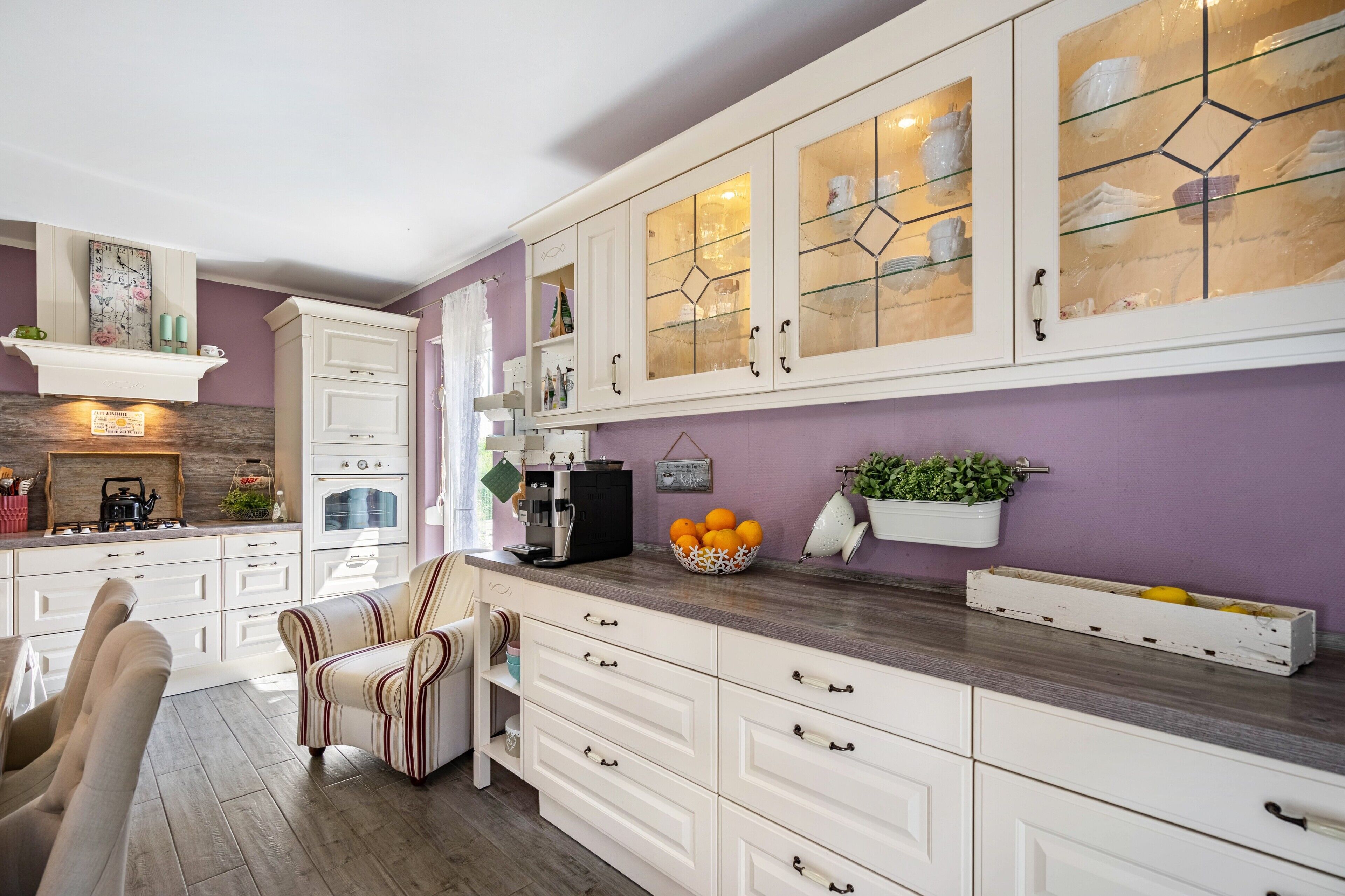 A kitchen with white cabinetry, a coffee machine, and a bowl of oranges on the counter.