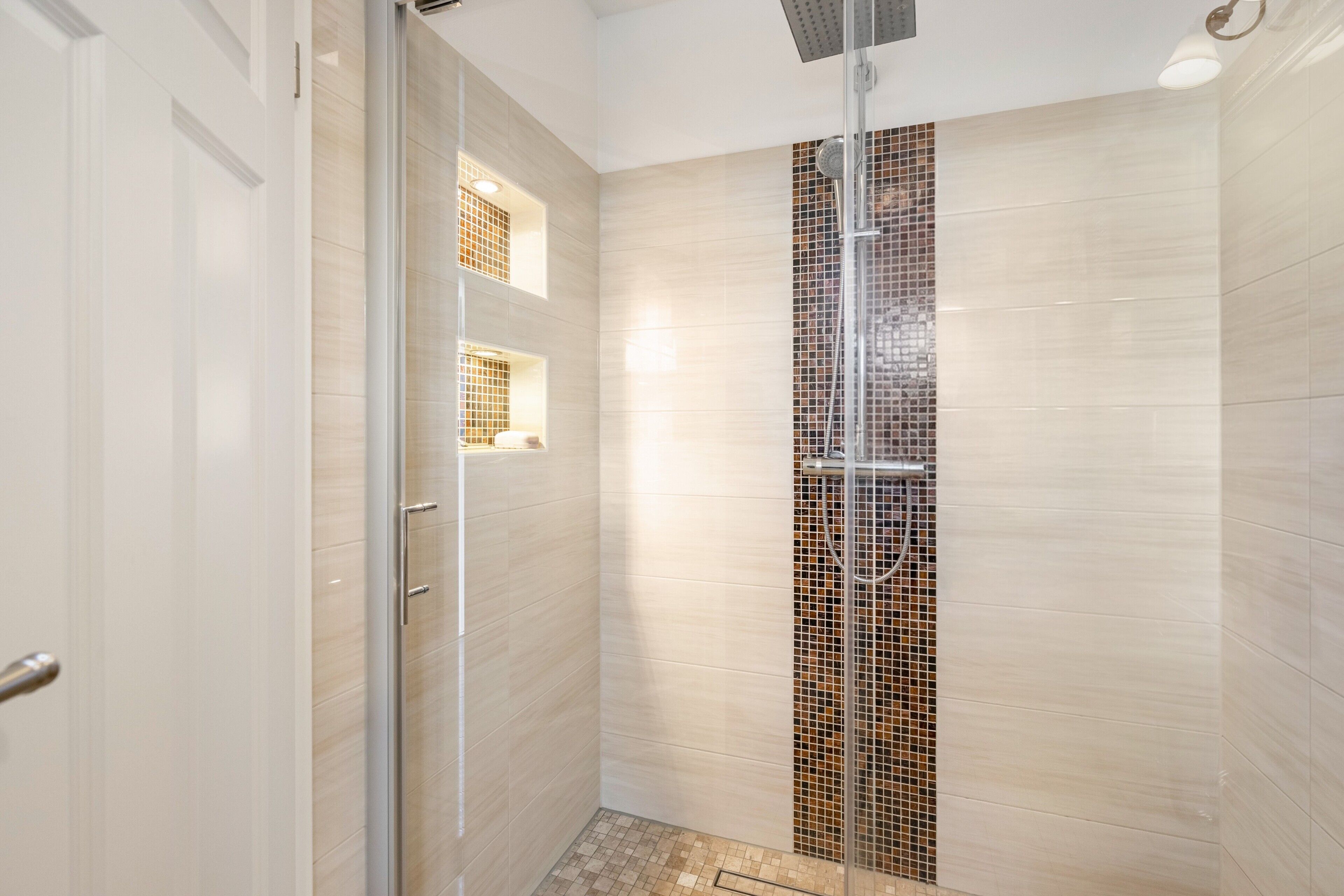 Ein modernes Badezimmer mit Duschkabine aus Glas, gefliesten Wänden und sichtbarer Toilette.