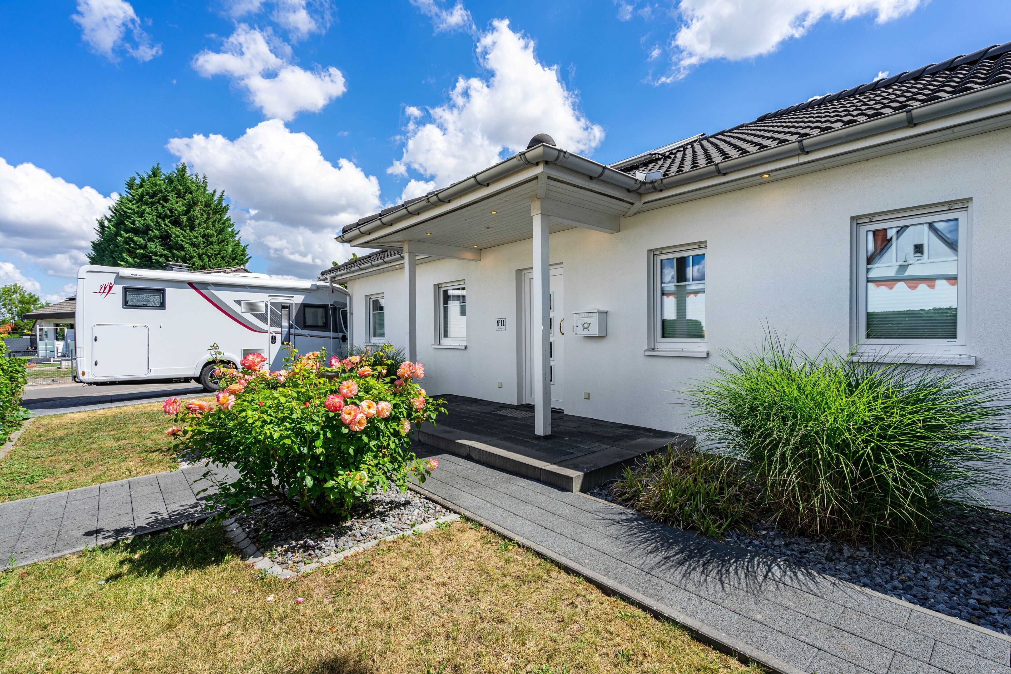 A single-story RV park building with a covered porch, a small garden with flowers, and a parked RV.