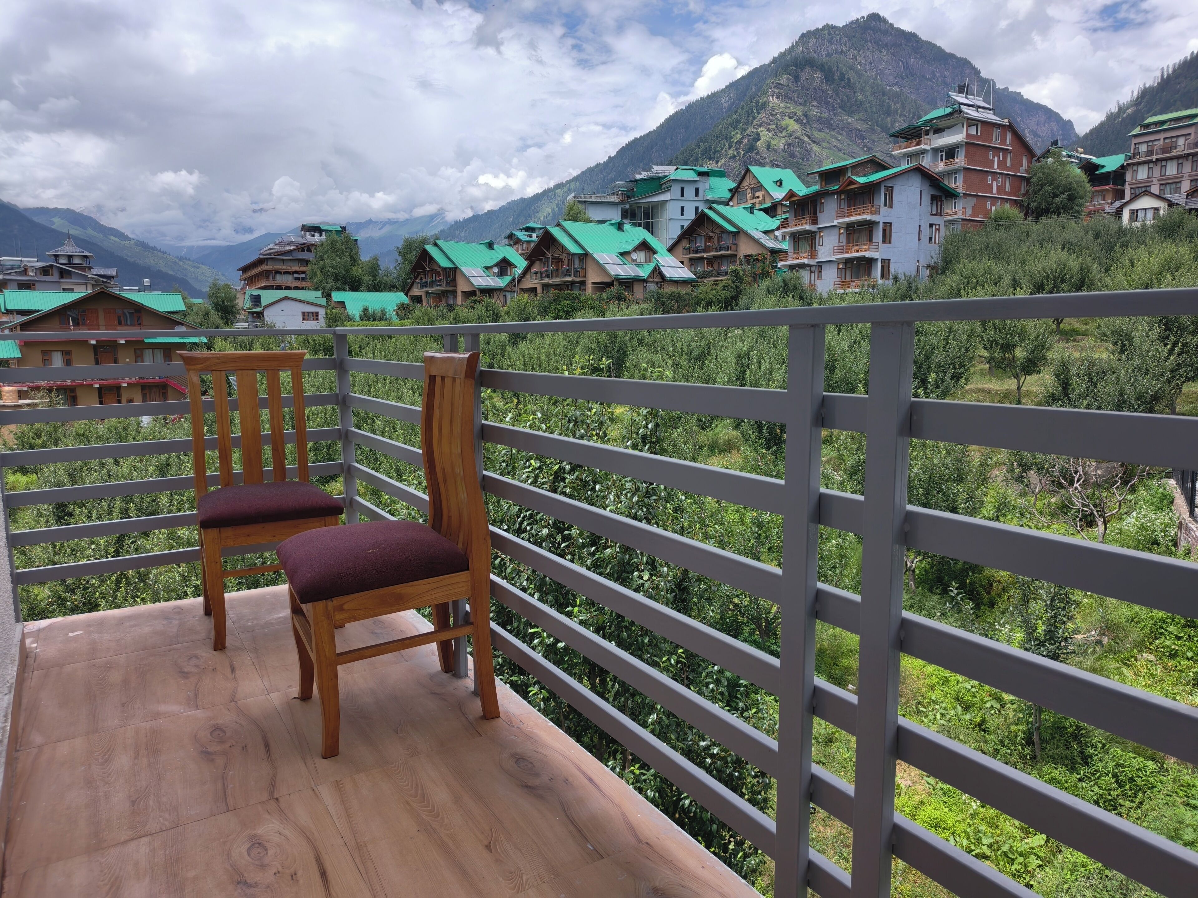 A balcony with a wooden chair, a railing, and a view of a mountainous area with buildings.