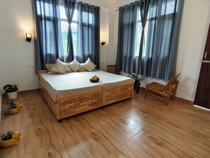 A bedroom with a large bed, wooden flooring, a small table, two chairs, and a potted plant.