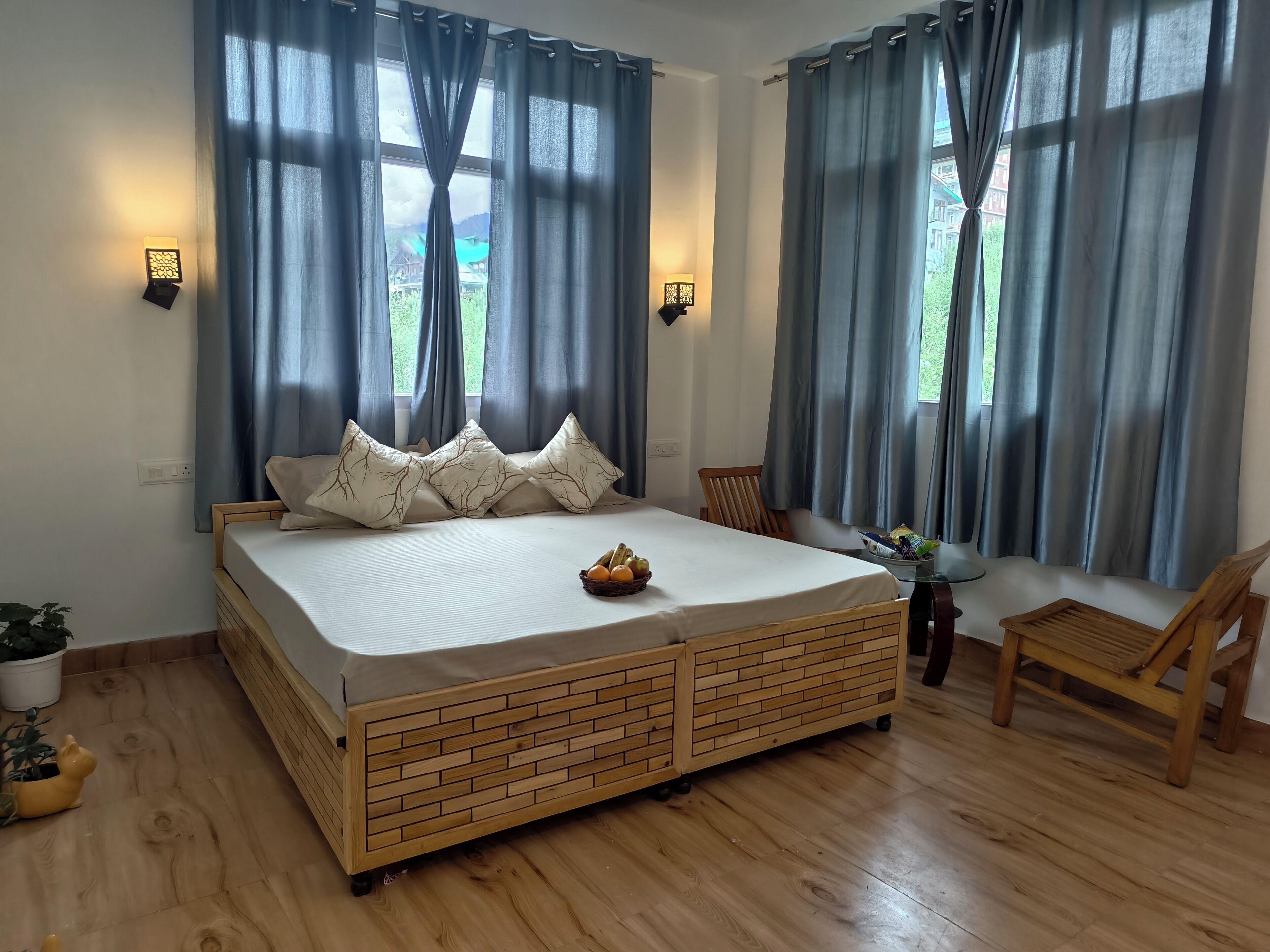 Een slaapkamer met een houten bed, twee nachtkastjes, een stoel en uitzicht op groen buiten.
