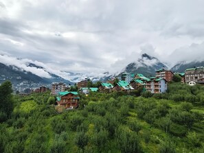 Ein dorfartige Siedlung in den Bergen mit traditioneller Architektur, üppigem Grün und schneebedeckten Berggipfeln im Hintergrund.