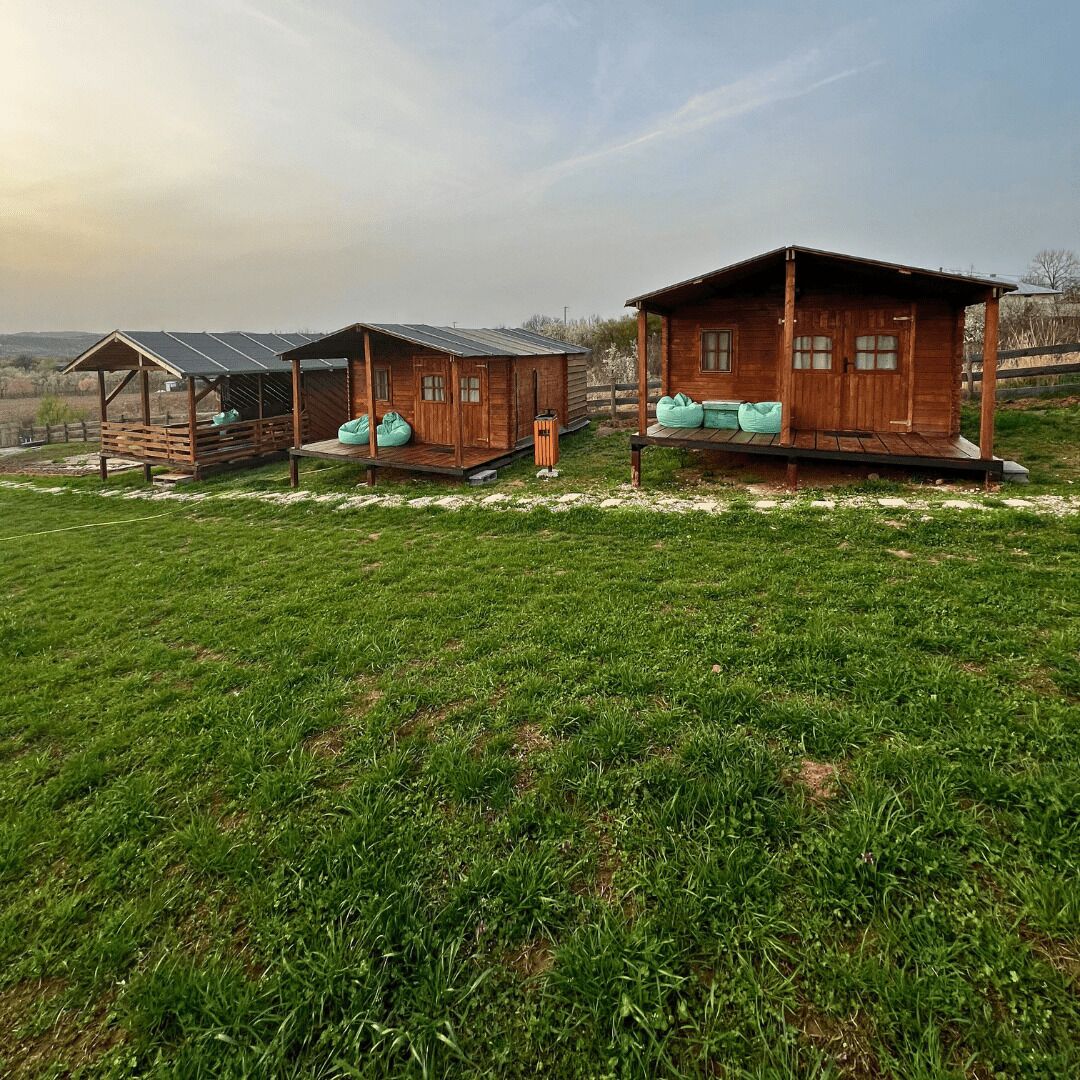 Una hilera de cabañas de madera con paneles solares, sillones de mimbre verdes y un campo cubierto de césped.