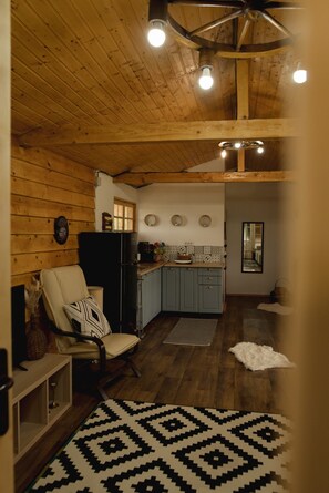 A cozy interior with a wooden ceiling, a kitchen area with cabinets and a refrigerator, a dining area with a chair and a rug.