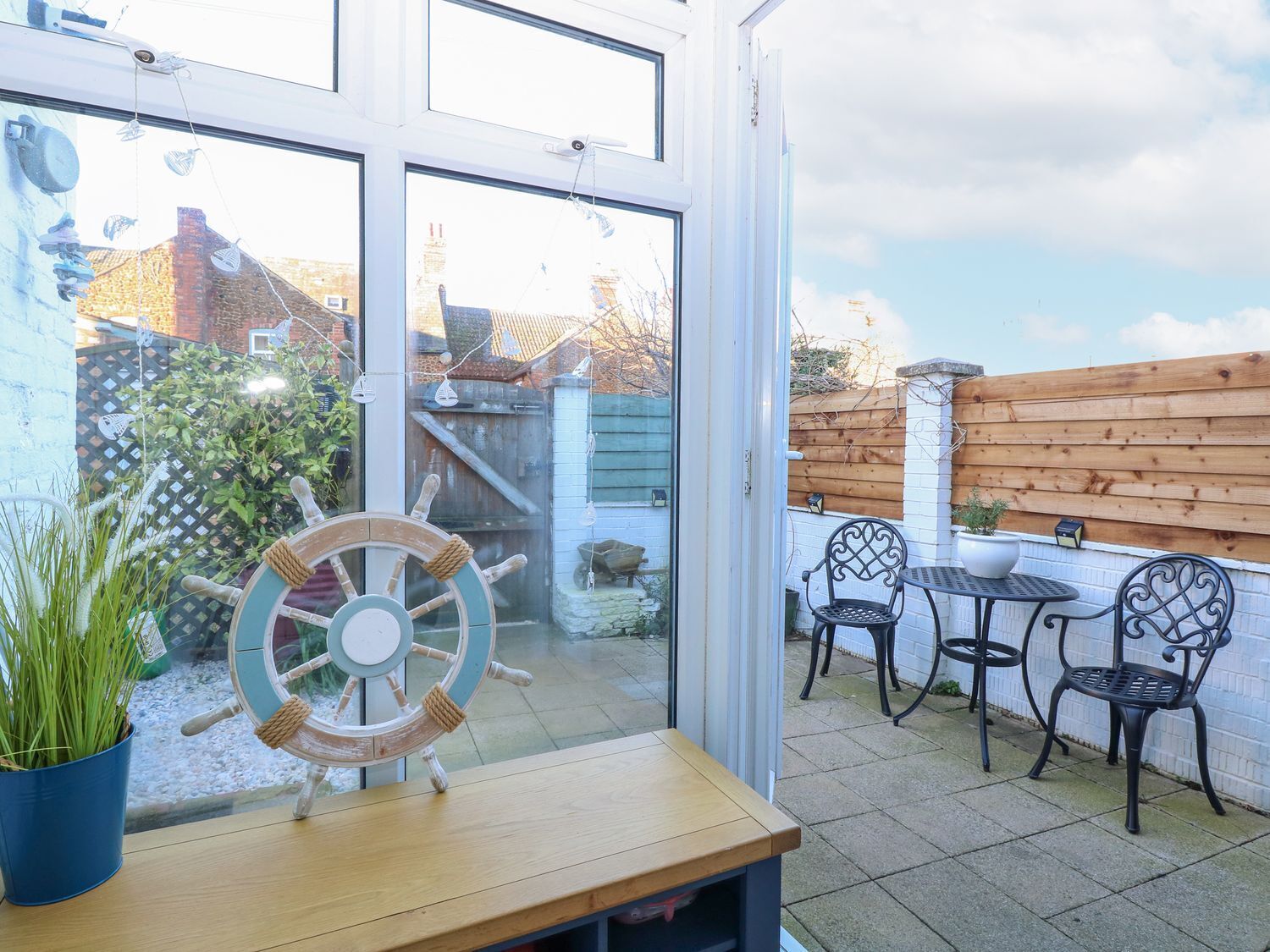 A patio with a wooden table and chairs, a ship's wheel decoration, and a view through a glass door.