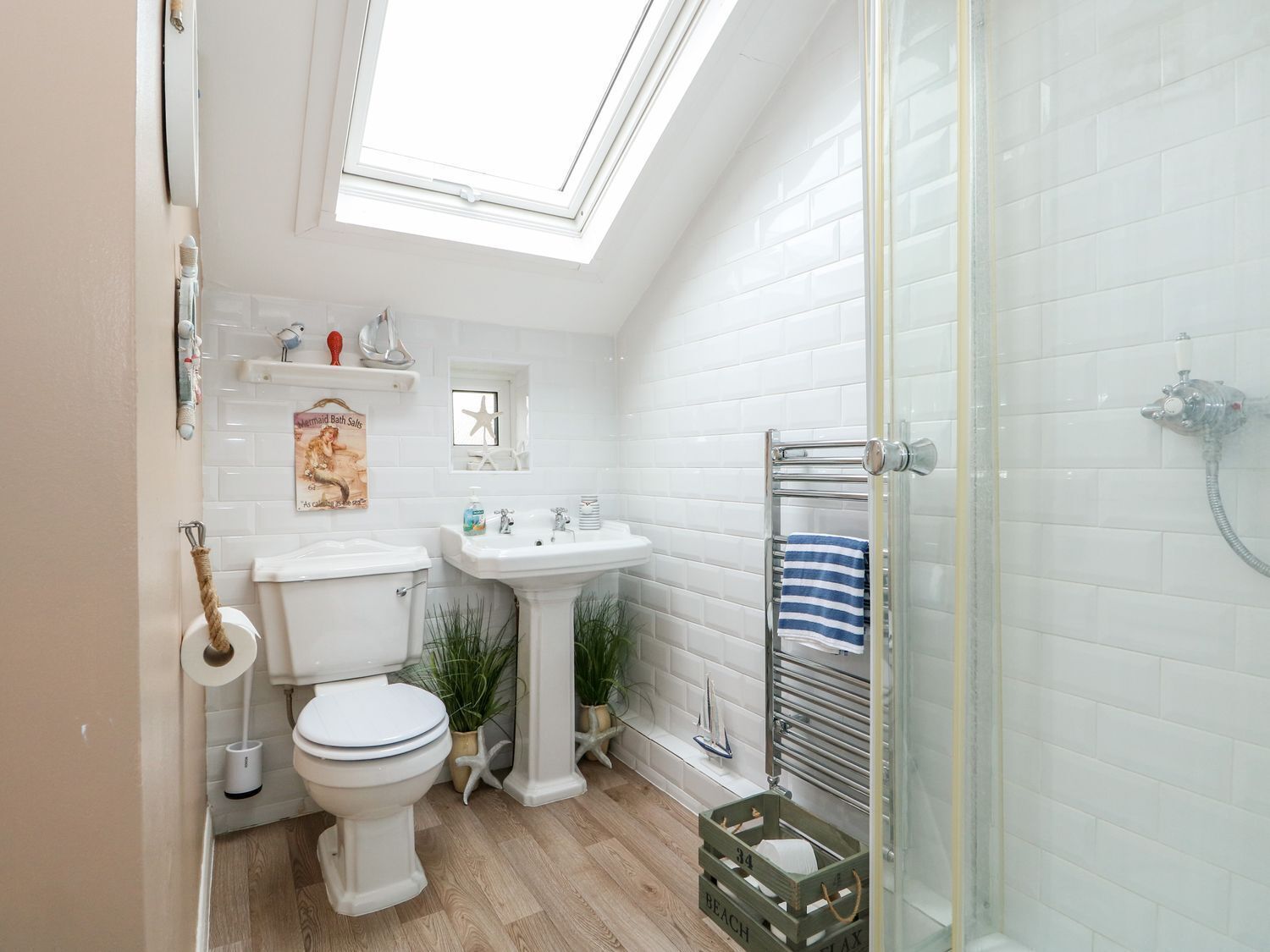A modern bathroom with a skylight, white tiles, a toilet, sink, and a shower.