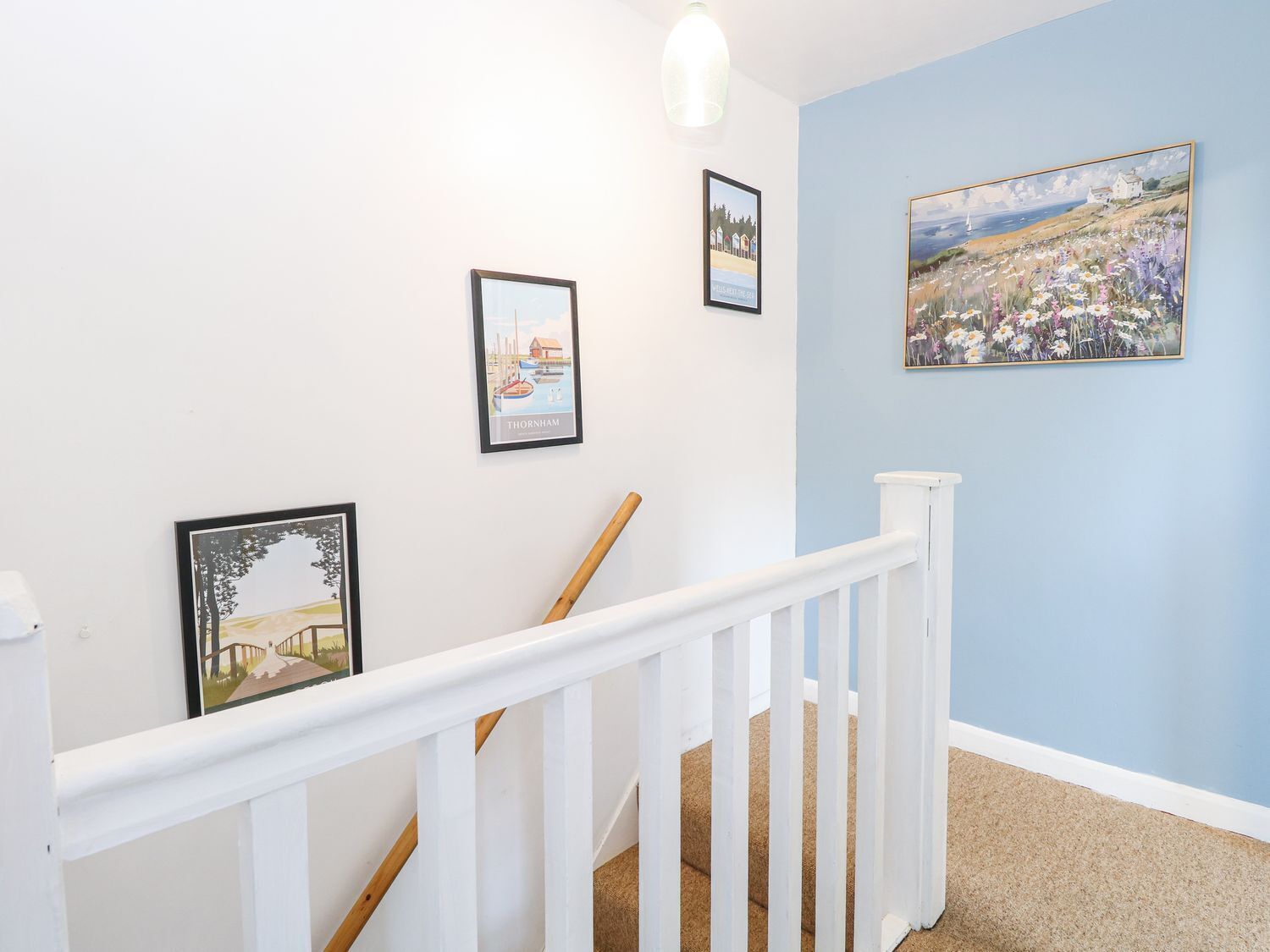 A staircase with white railings and a blue wall. There are three framed pictures on the wall.