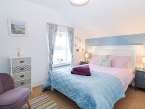 A bedroom with a bed, a dresser, a chair, and a window with curtains. - Hideaway Cottage (Hunstanton)